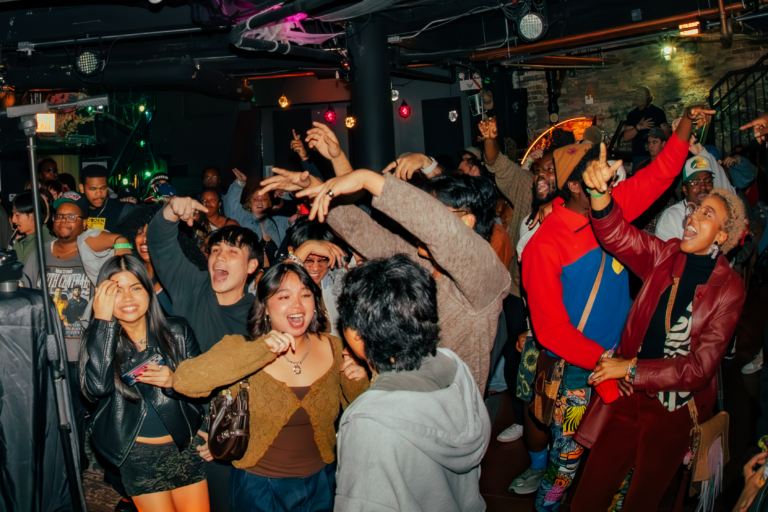 Brightly lit crowd with their arms raised in the downstairs venue